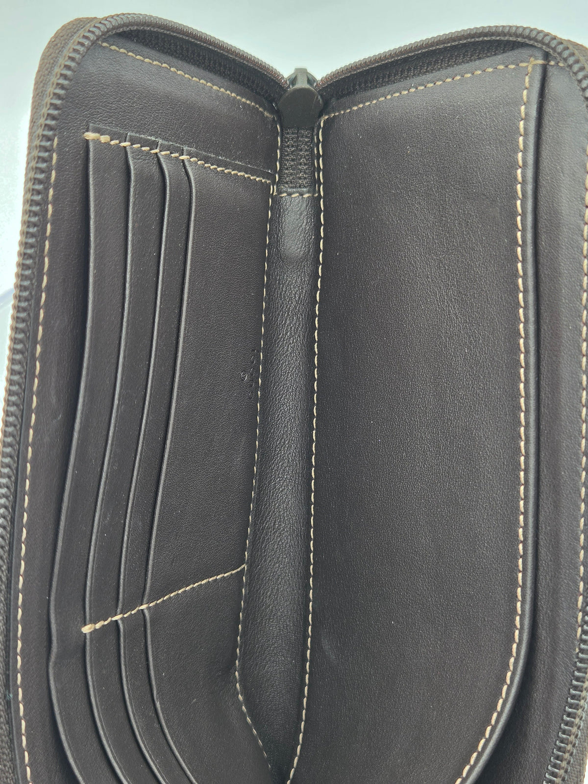 Close-up of an open black leather zip-around wallet showing the interior card slots, center divider, and contrast light tan stitching.