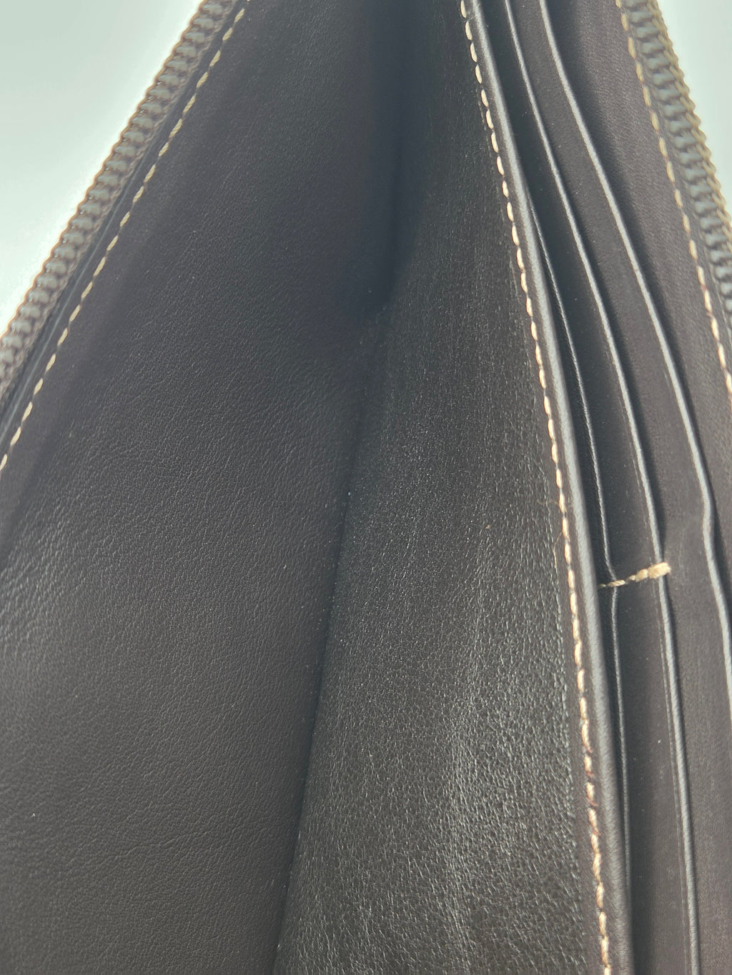 Close-up of the interior of a dark brown leather wallet or clutch, showing the textured leather lining, card slots, and light beige contrast stitching.