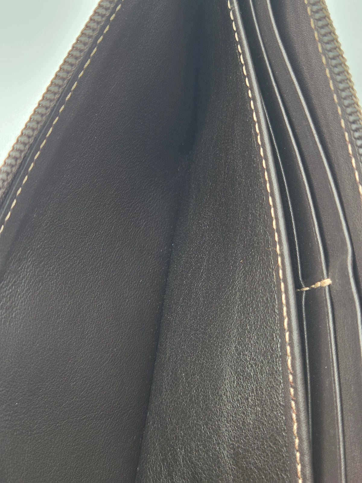 Close-up of the interior of a dark brown leather wallet or clutch, showing the textured leather lining, card slots, and light beige contrast stitching.