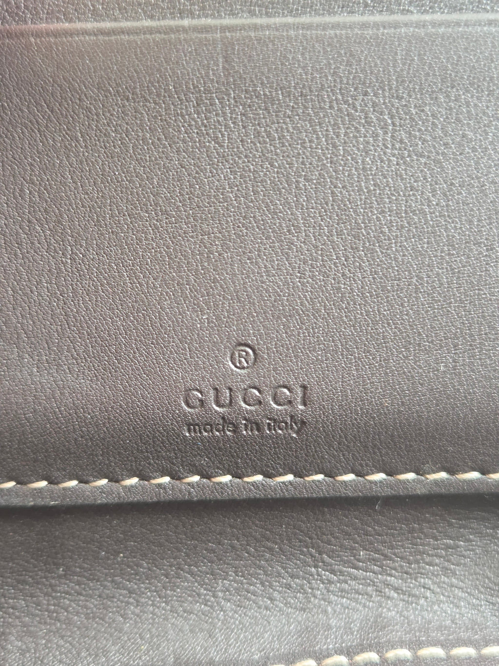 Close-up of a dark gray textured leather item with white stitching and an embossed GUCCI logo with 'made in Italy' on the front.