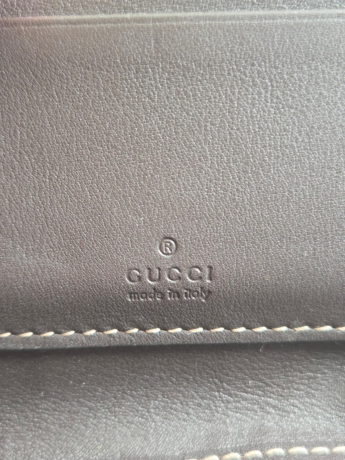 Close-up of a dark gray textured leather item with white stitching and an embossed GUCCI logo with 'made in Italy' on the front.