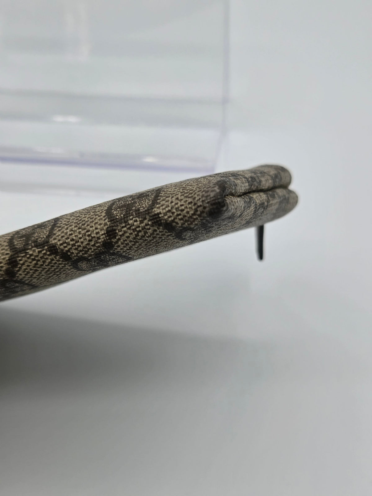 A close-up of a snake with a brown and beige patterned body and a dark tail tip, resting on a light gray surface.