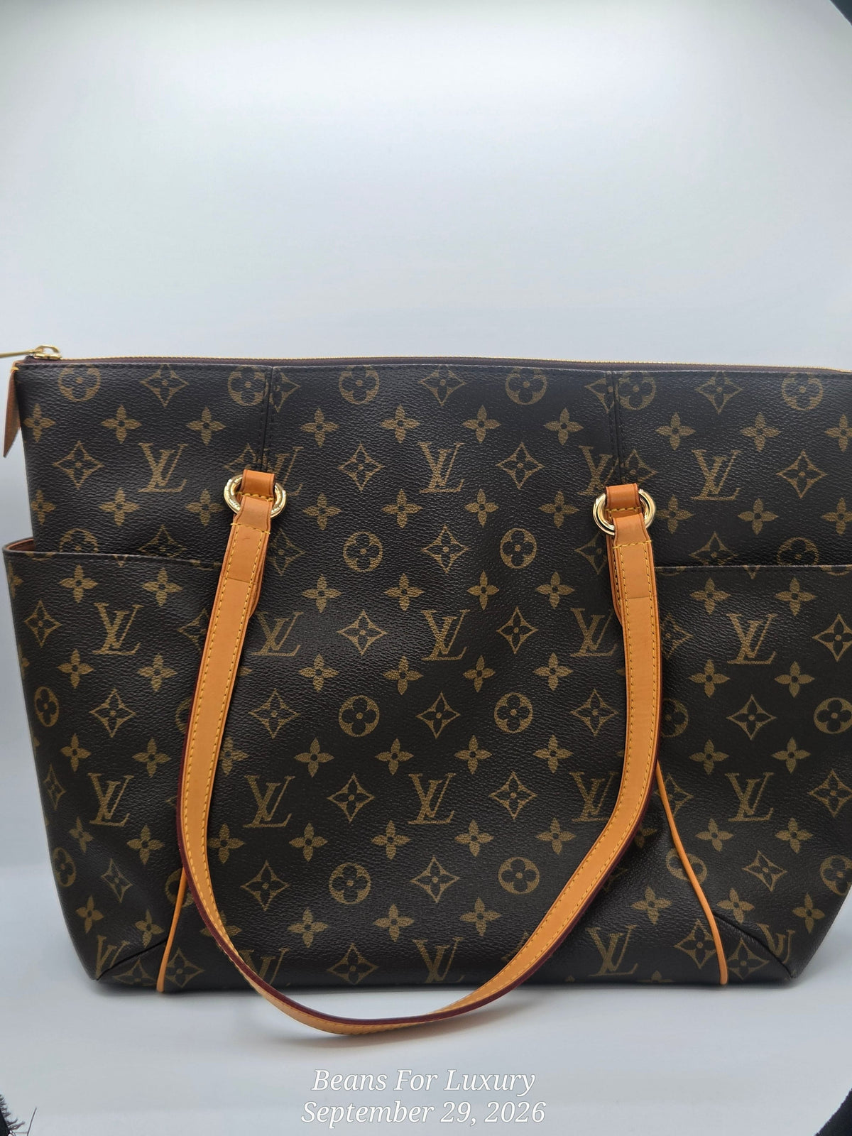 A Louis Vuitton monogram canvas tote bag with tan leather handles and gold-tone hardware, photographed against a white studio background with a black vignette at the corners.