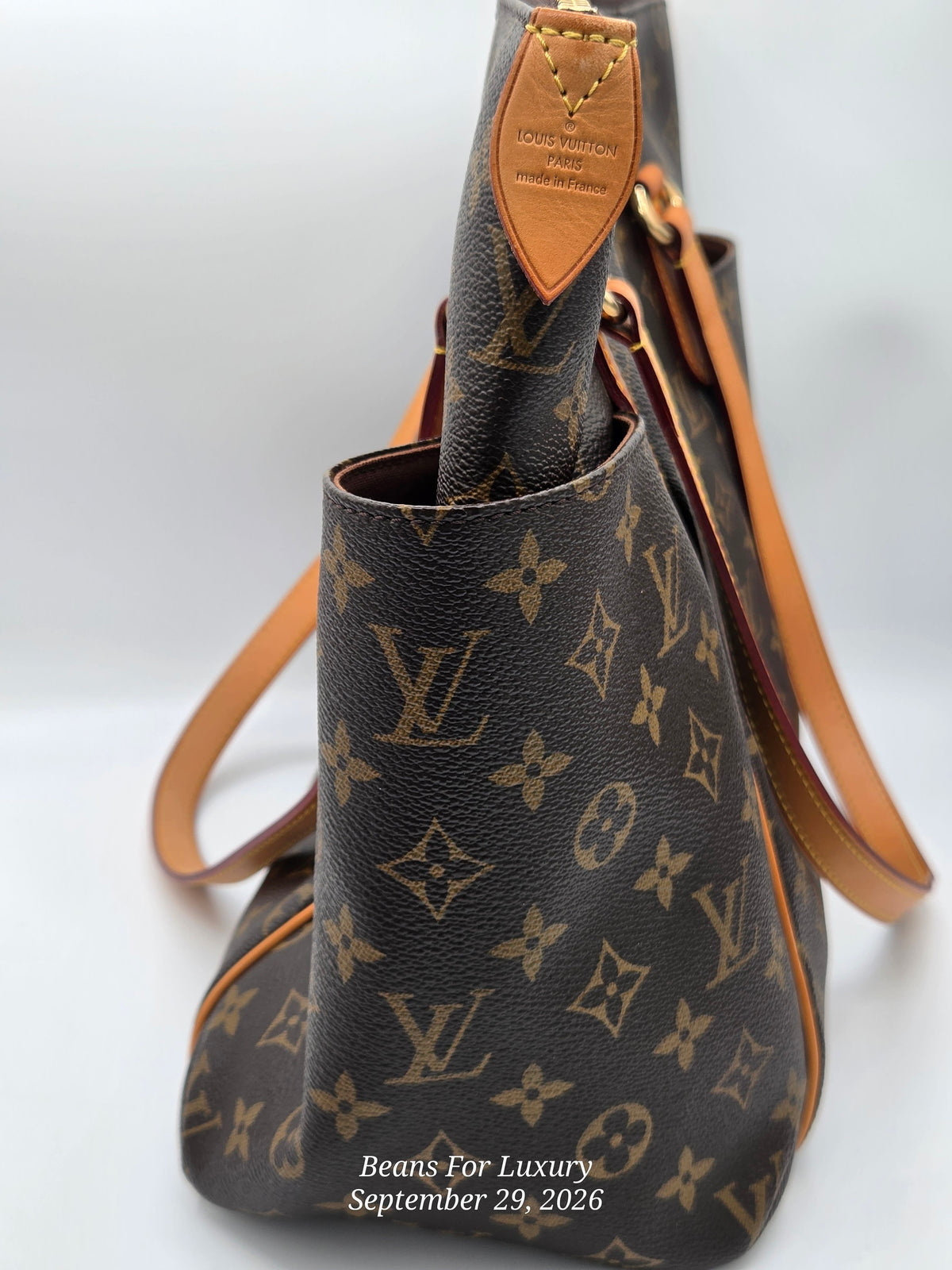 Louis Vuitton monogram canvas shoulder bag in dark brown with tan leather trim and strap, shown against a light gray background. A Louis Vuitton leather tab is visible near the top handle, and the brand name 'Beans For Luxury' with a date watermark is printed at the bottom.