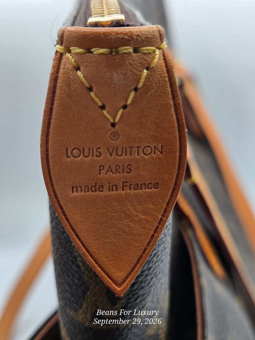 Close-up of a Louis Vuitton leather tag on a dark brown monogram bag, showing the embossed text 'LOUIS VUITTON PARIS made in France' with gold stitching.