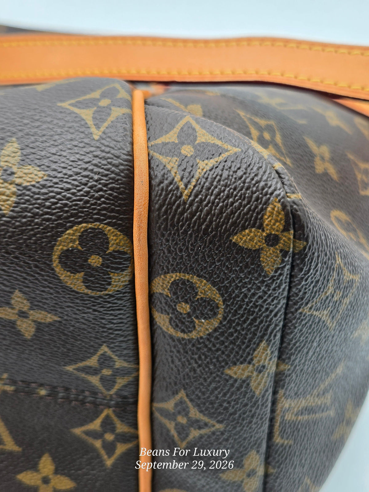Close-up of a Louis Vuitton monogram bag corner showing dark brown coated canvas with tan/gold LV monogram pattern and orange-brown leather trim.