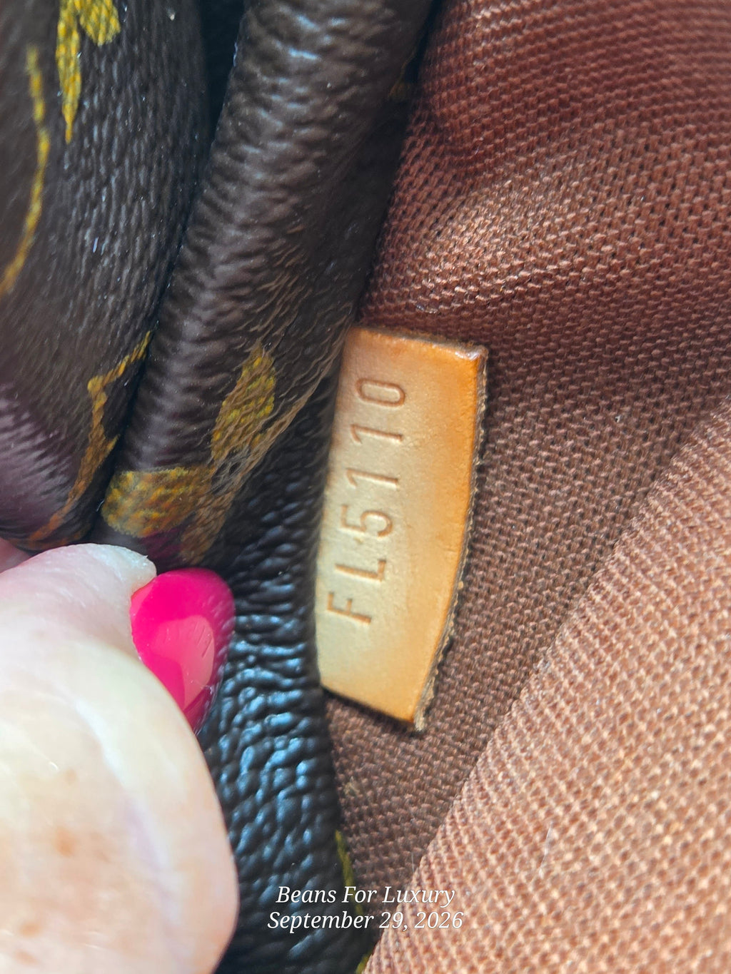 Close-up of a Louis Vuitton monogram bag interior showing a tan leather tag with the embossed code FL5110, with a hand pointing at it.