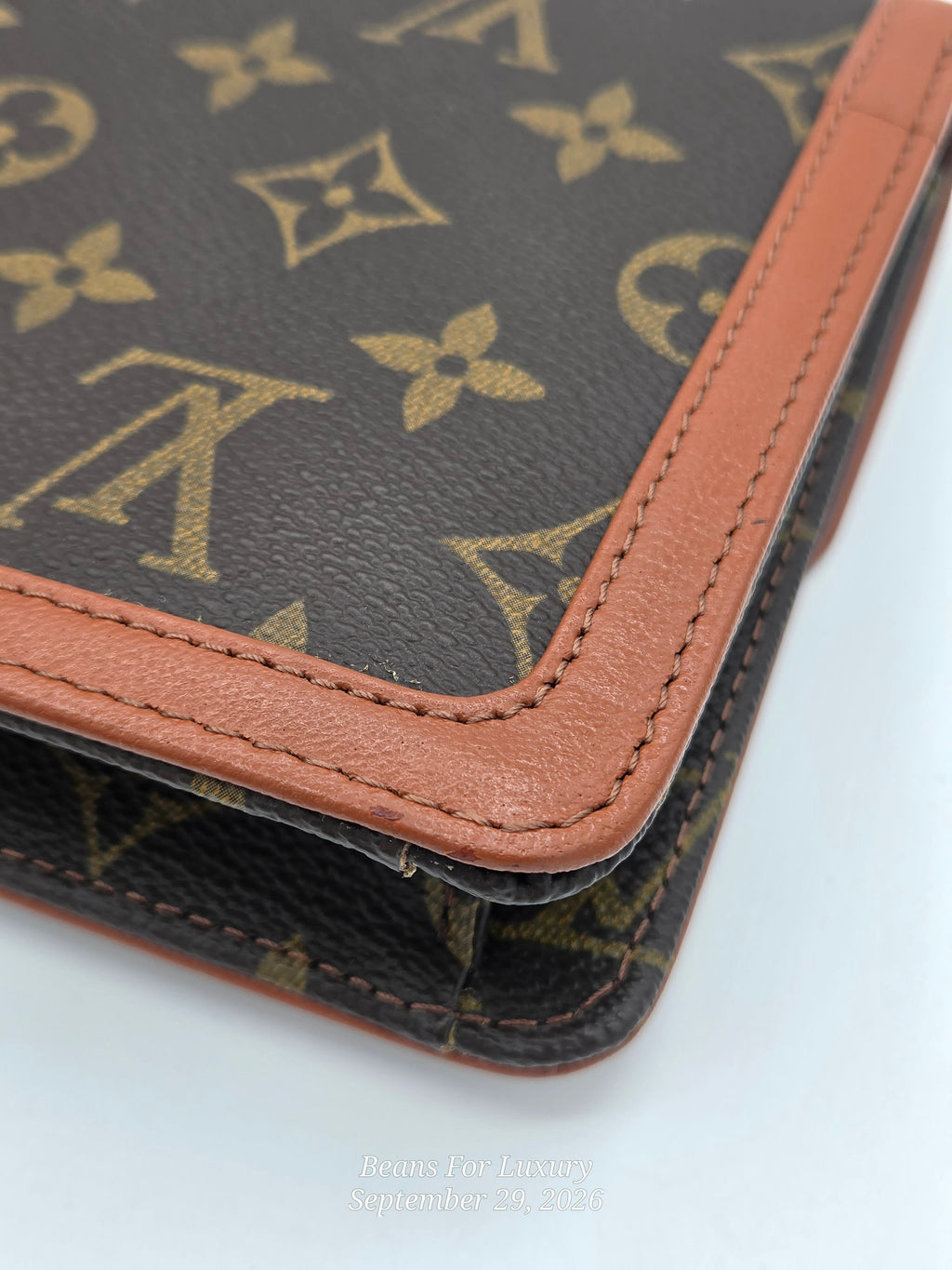 Close-up of a Louis Vuitton monogram canvas item with tan leather trim and stitching, showing the classic dark brown coated canvas with gold-tone LV monogram pattern and a tan leather border.