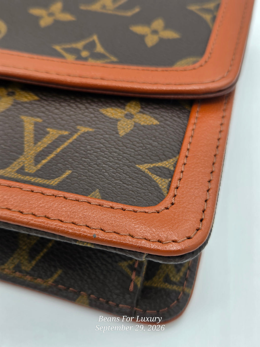 Close-up of a Louis Vuitton monogram pouch or wallet showing the classic brown coated canvas with gold LV monogram pattern and contrasting tan leather trim.