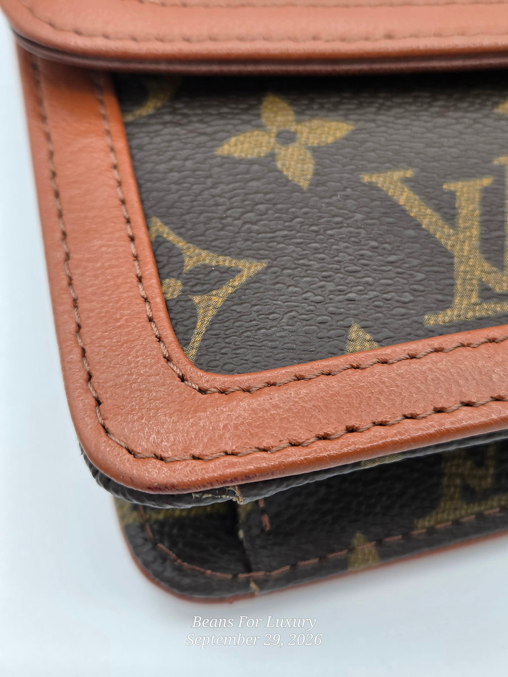 Close-up of a Louis Vuitton monogram wallet or card holder showing the dark brown coated canvas with tan monogram print and a tan leather border with visible stitching.