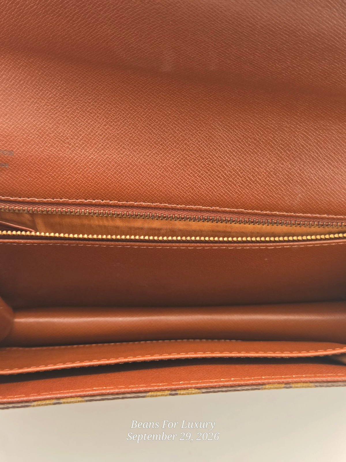 Close-up of the interior of a brown textured leather bag, showing a zippered compartment and card slots, with a small watermark at the bottom reading 'Beans For Luxury September 29, 2026'.