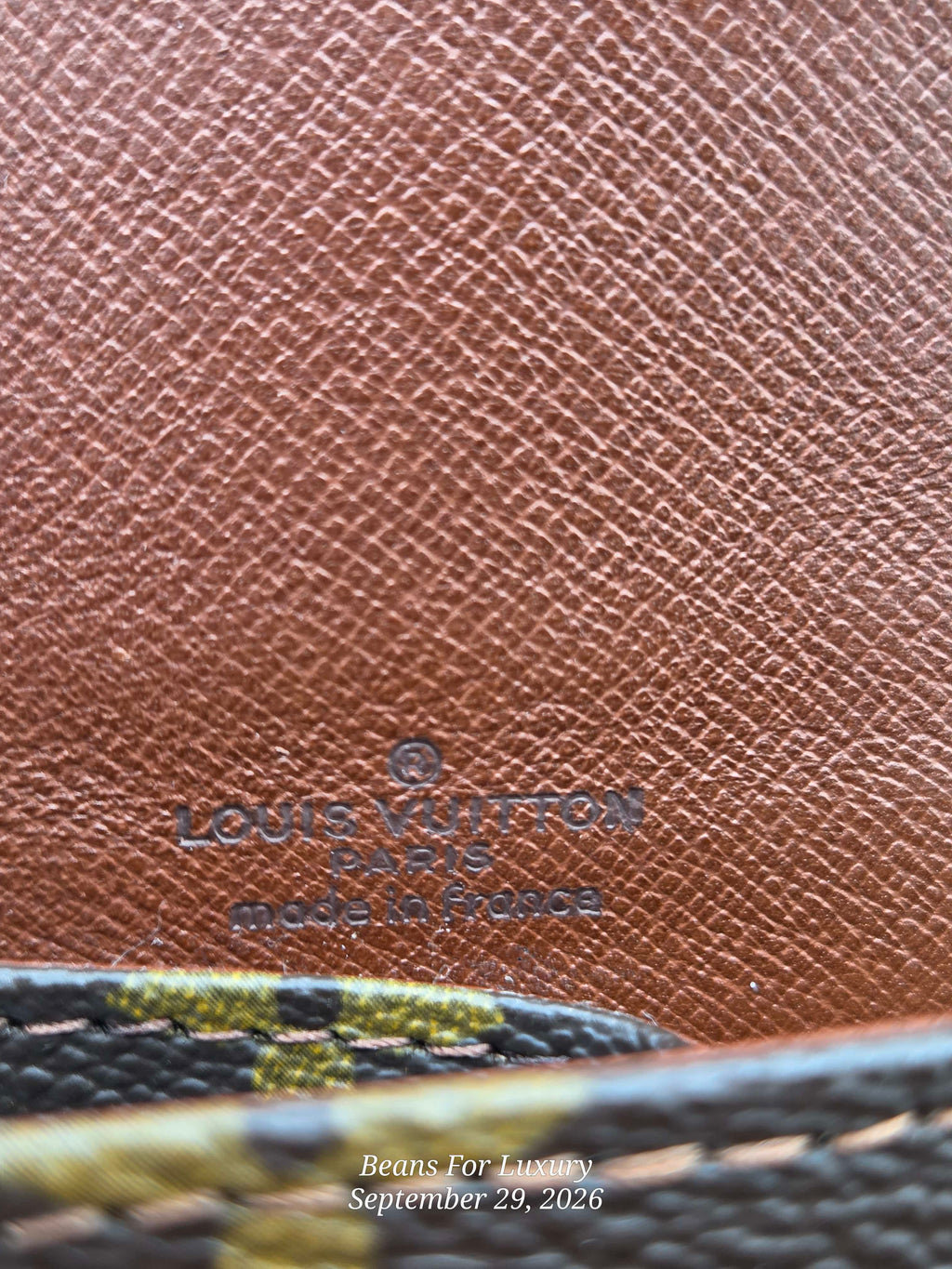 Close-up of a brown textured leather interior with embossed Louis Vuitton Paris branding and a patterned fabric edge at the bottom.