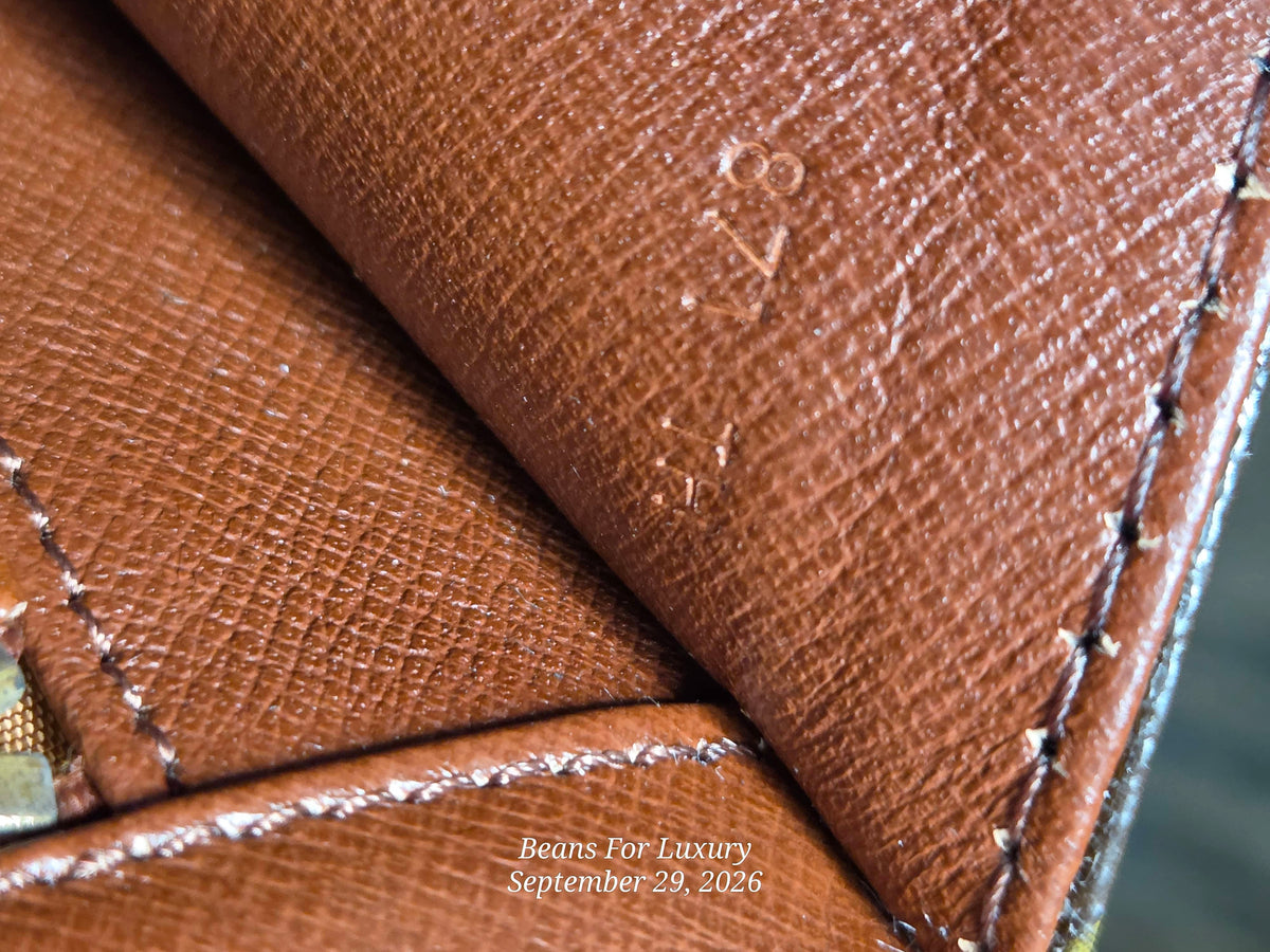 Close-up of a brown textured leather item, showing grain, stitching, and an embossed serial number, with a small watermark reading Beans For Luxury.