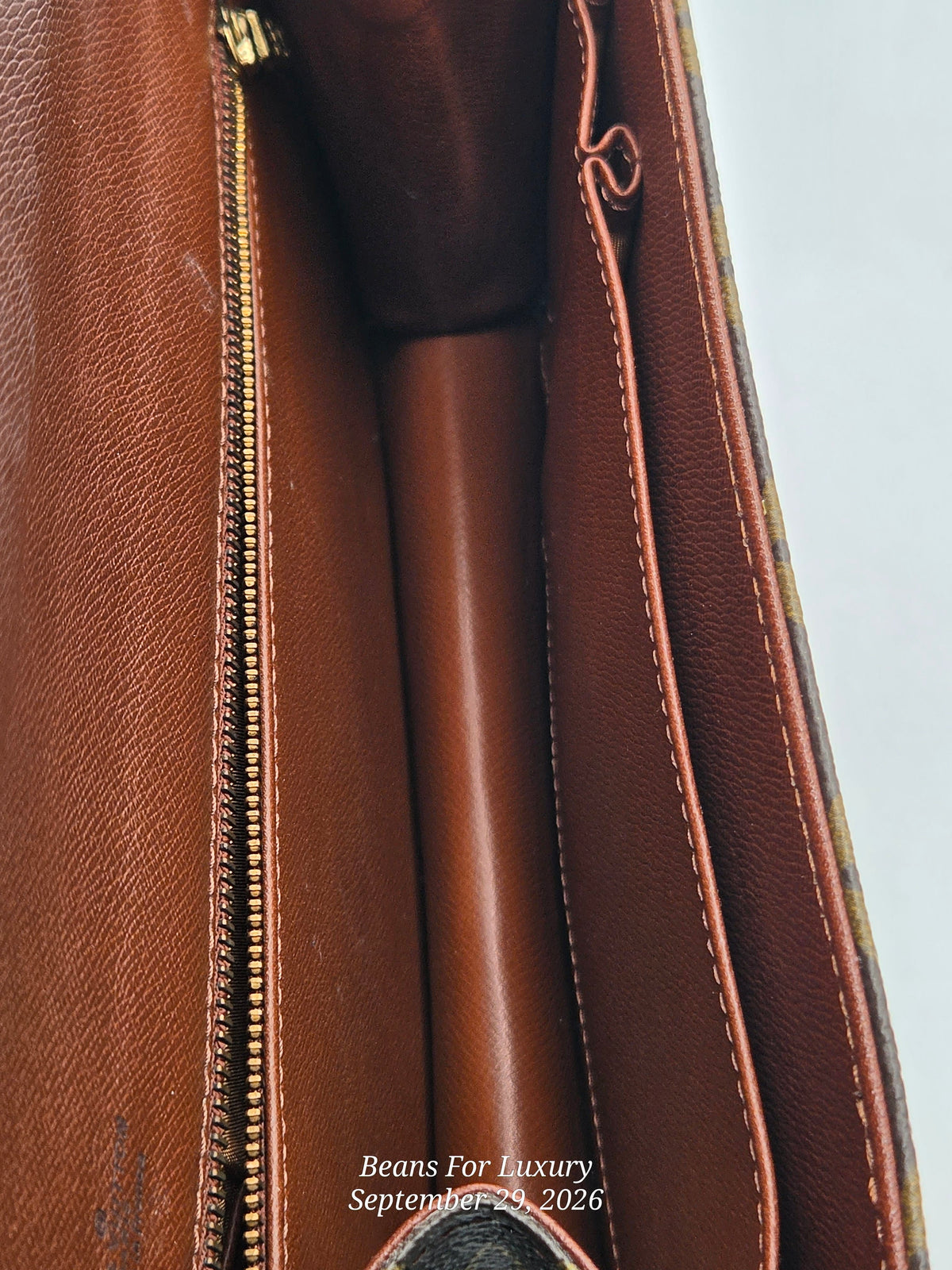 Close-up detail of a brown leather bag interior showing a gold zipper, stitched pocket, and smooth brown lining, with a small watermark reading Beans For Luxury September 25 2026.