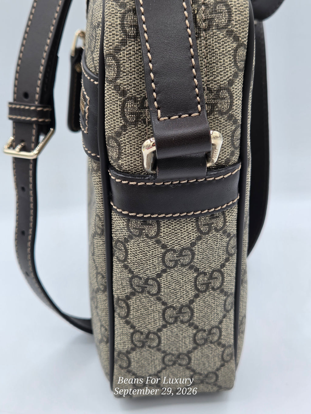 Close-up of a Gucci monogram canvas shoulder bag with dark brown leather trim and strap, gold-tone hardware, and contrast stitching on a light gray background.