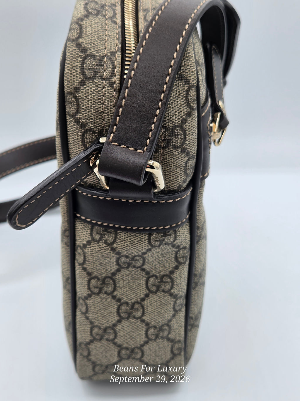 A close-up side view of a Gucci crossbody bag in the classic GG Supreme canvas, featuring dark brown leather trim, gold-tone hardware, and white contrast stitching. A watermark for 'Beans For Luxury' is visible at the bottom.