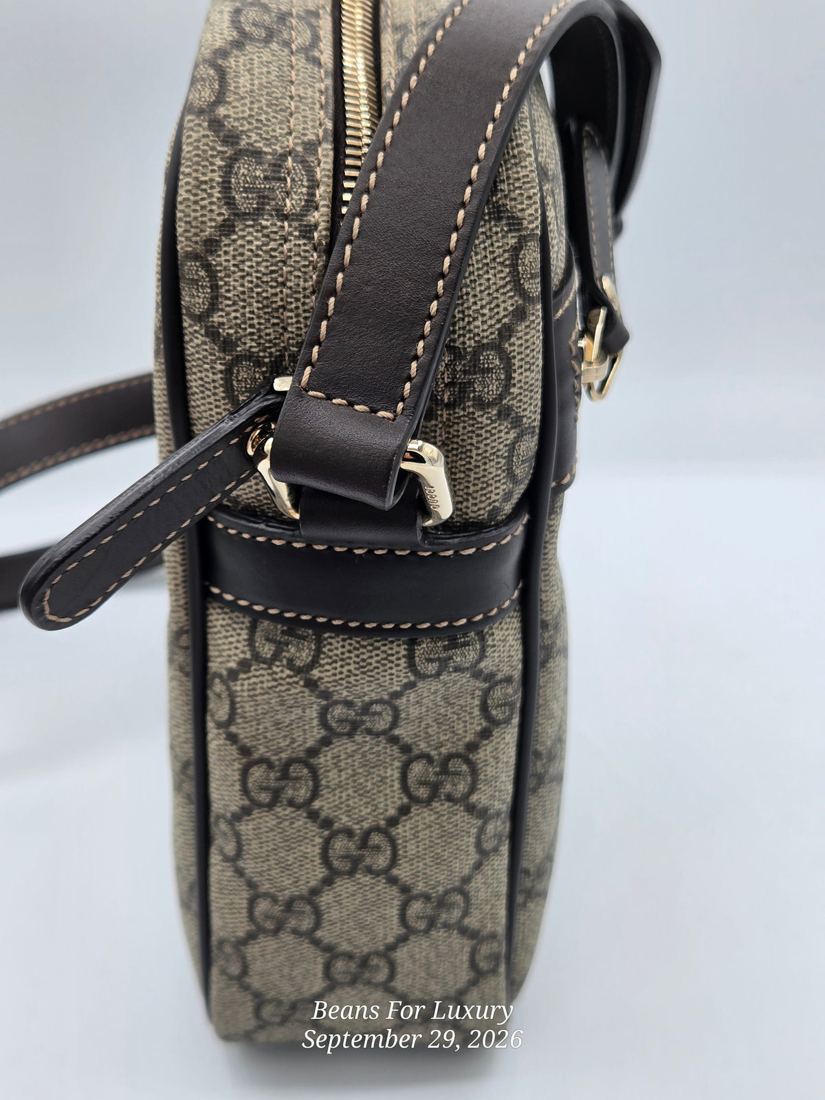 A close-up side view of a Gucci crossbody bag in the classic GG Supreme canvas, featuring dark brown leather trim, gold-tone hardware, and white contrast stitching. A watermark for 'Beans For Luxury' is visible at the bottom.