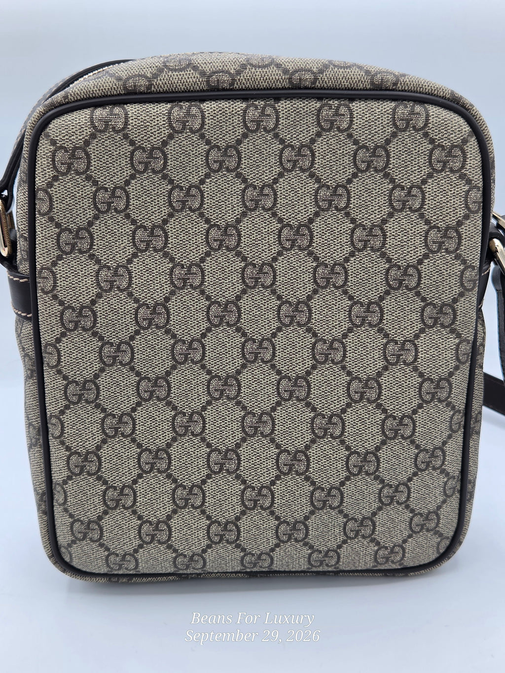A small crossbody bag featuring the classic beige and brown GG Supreme monogram canvas. The bag has a structured rectangular shape with a black zipper and a black leather strap, shown against a light gray background.