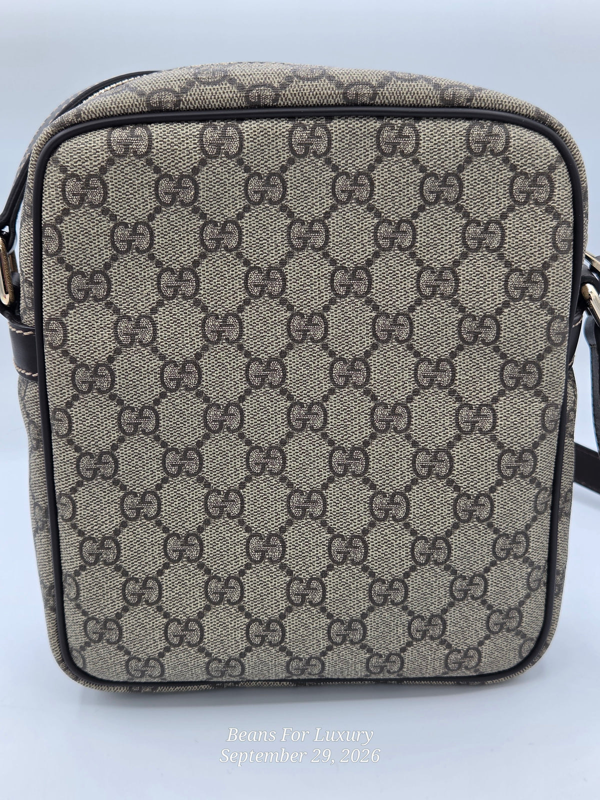 A small crossbody bag featuring the classic beige and brown GG Supreme monogram canvas. The bag has a structured rectangular shape with a black zipper and a black leather strap, shown against a light gray background.