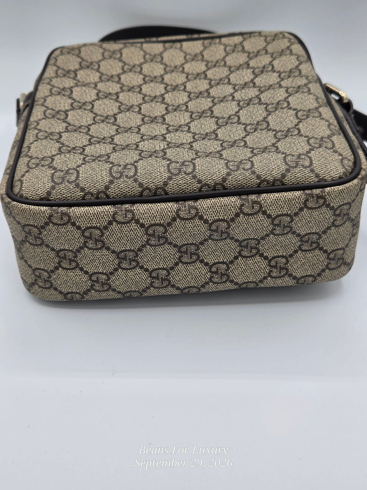 A small rectangular shoulder bag in beige and brown GG Supreme canvas with black trim and a black strap, photographed on a white background.