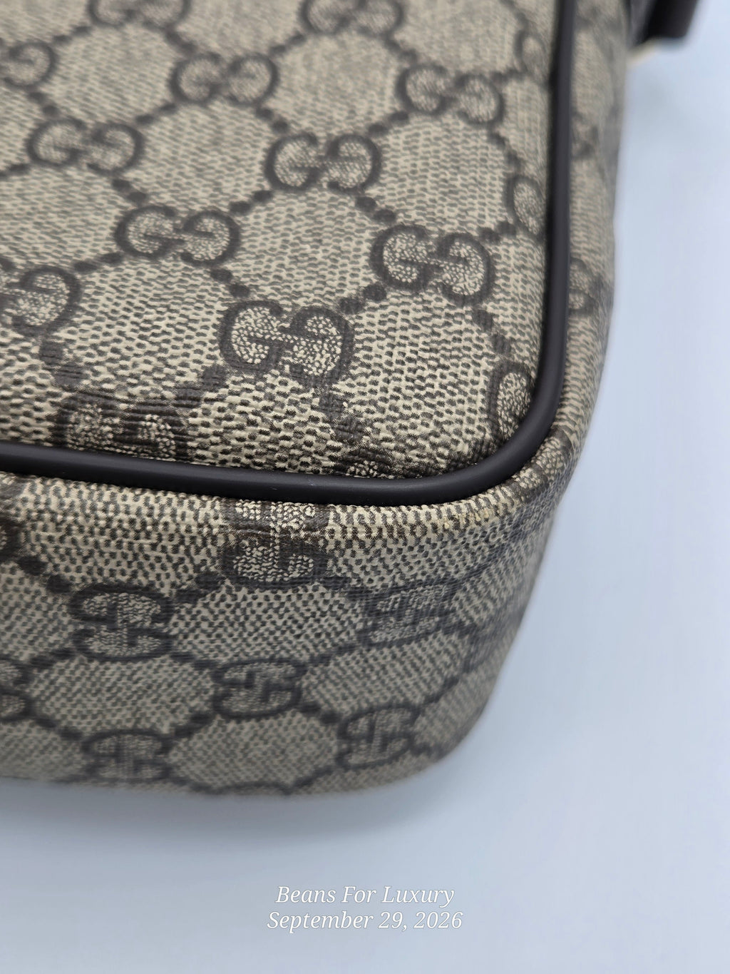 Close-up of a beige and black monogram canvas bag corner with black piping, showing the repeating interlocking GG pattern.