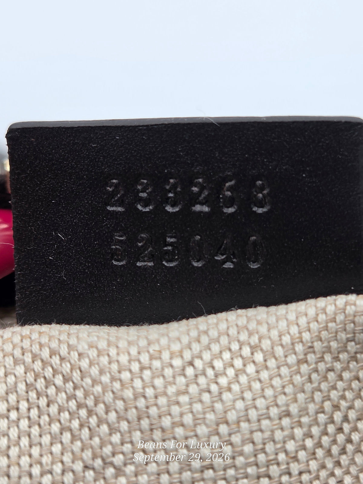 Close-up of a black leather patch stamped with the numbers '233268' and '525040', resting on a beige woven fabric surface against a light blue background.