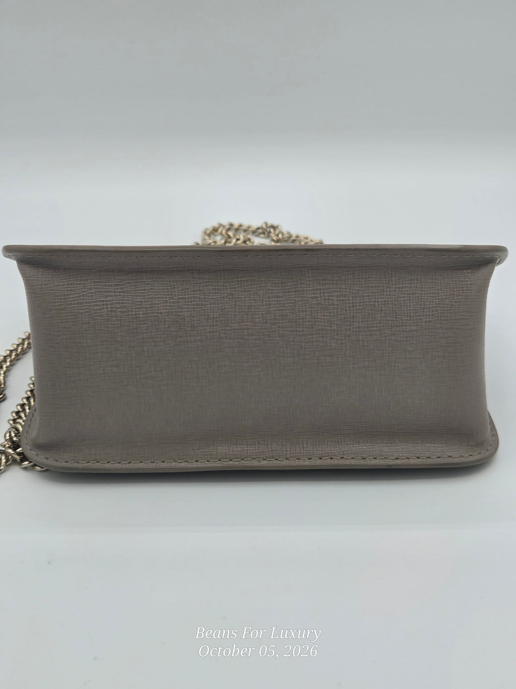 A taupe leather shoulder bag with a gold chain strap, shown from the front on a light gray background.