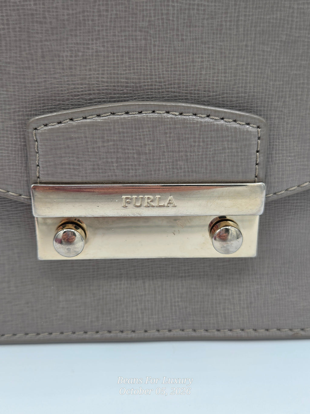 Close-up of a Furla handbag in textured gray leather with a polished silver-tone metal clasp engraved with the FURLA brand name.