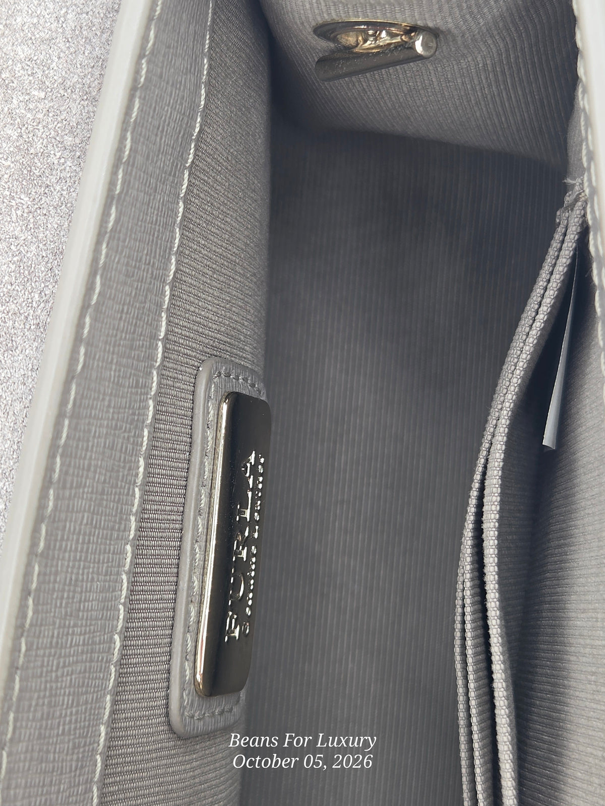 Close-up of the interior lining of a gray textured handbag, showing a zippered compartment, stitched edge, and a small metal brand plaque. The text 'Beans For Luxury' is visible on the plaque and as a watermark at the bottom.
