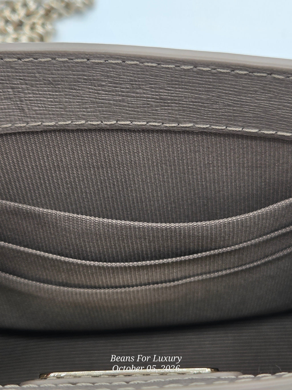 Close-up detail of a gray fabric interior with stitched compartments and a small metal clasp, with a faint watermark reading Beans For Luxury at the bottom.