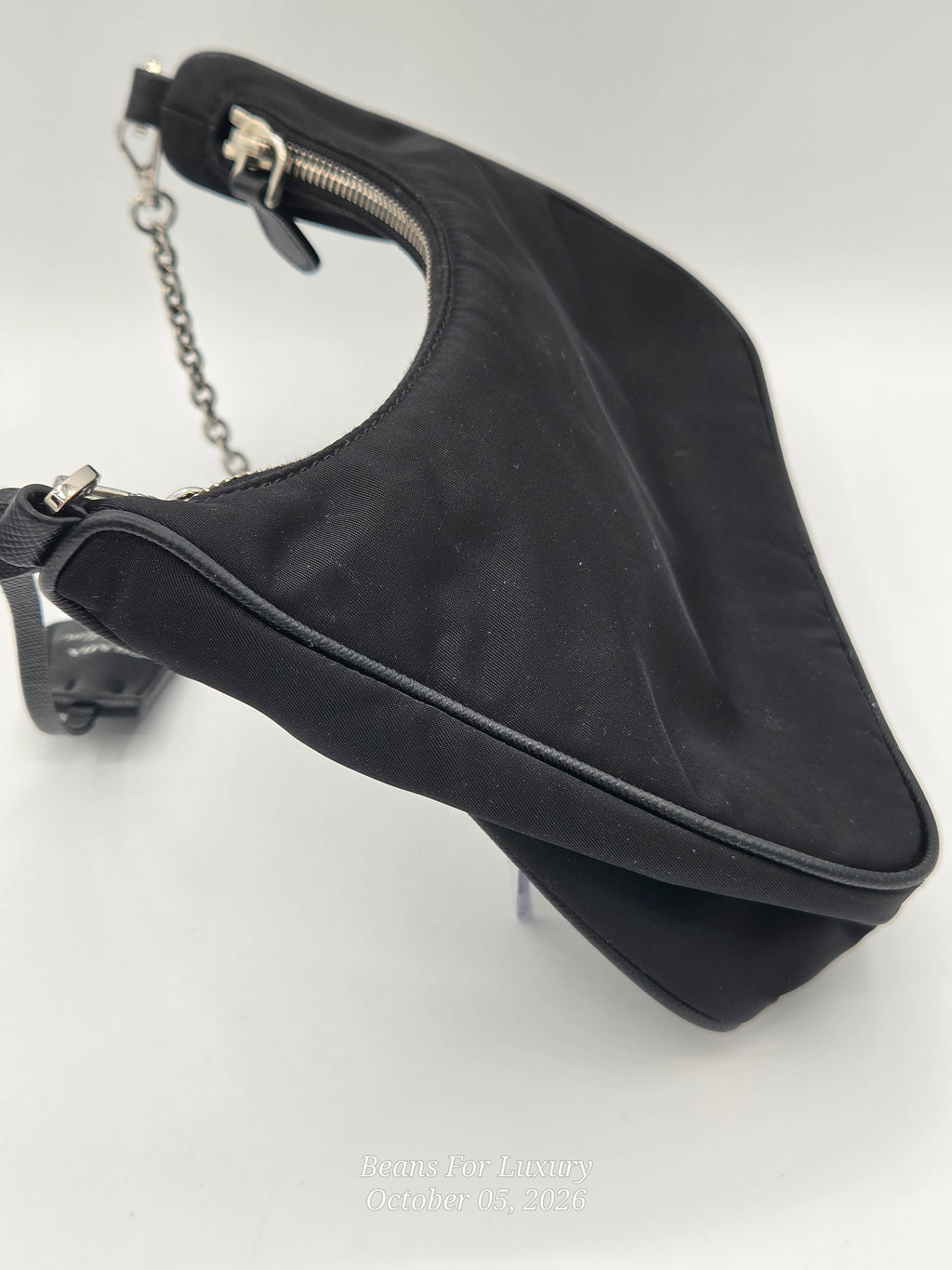 A black nylon shoulder bag with a silver chain strap and silver zipper, photographed on a light gray background.