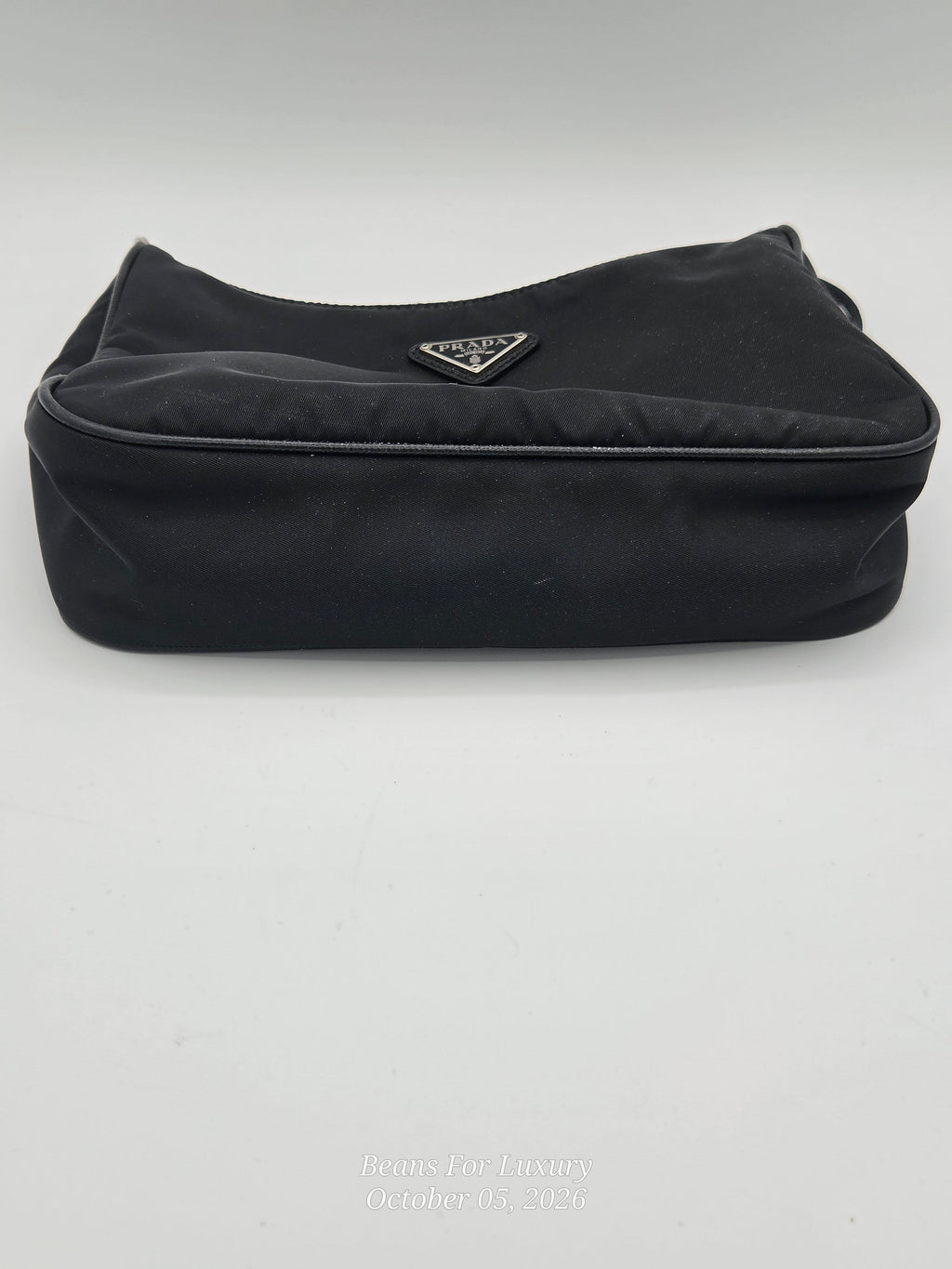 A black Prada nylon pouch bag with the signature silver-tone triangular Prada logo plaque on the front, set against a plain light gray background.