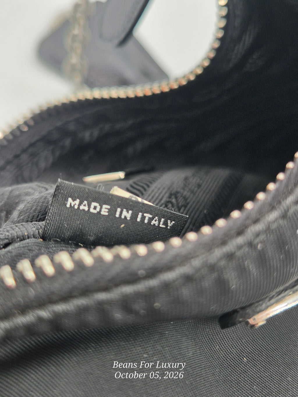 Close-up of the interior of a black fabric bag showing a sewn-in label that reads 'MADE IN ITALY' with a silver zipper around the opening.