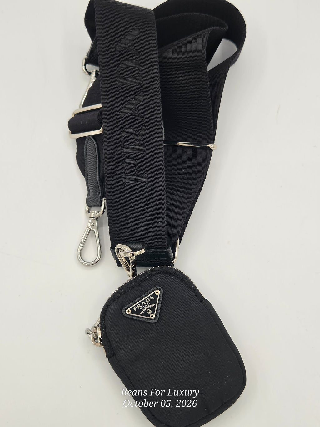 A black Prada crossbody bag with a matching adjustable black webbing strap featuring the embossed Prada logo and silver-tone hardware, shown on a plain white background.