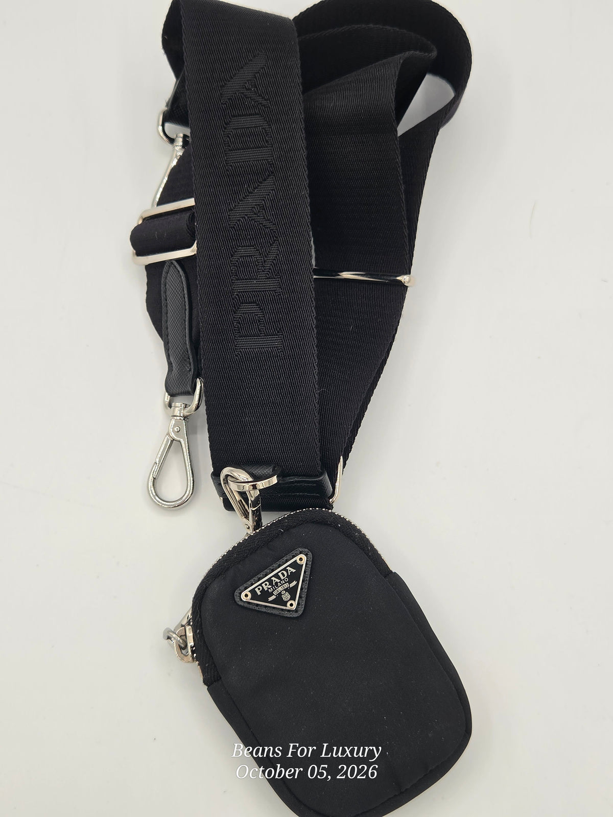A black Prada crossbody bag with a matching adjustable black webbing strap featuring the embossed Prada logo and silver-tone hardware, shown on a plain white background.