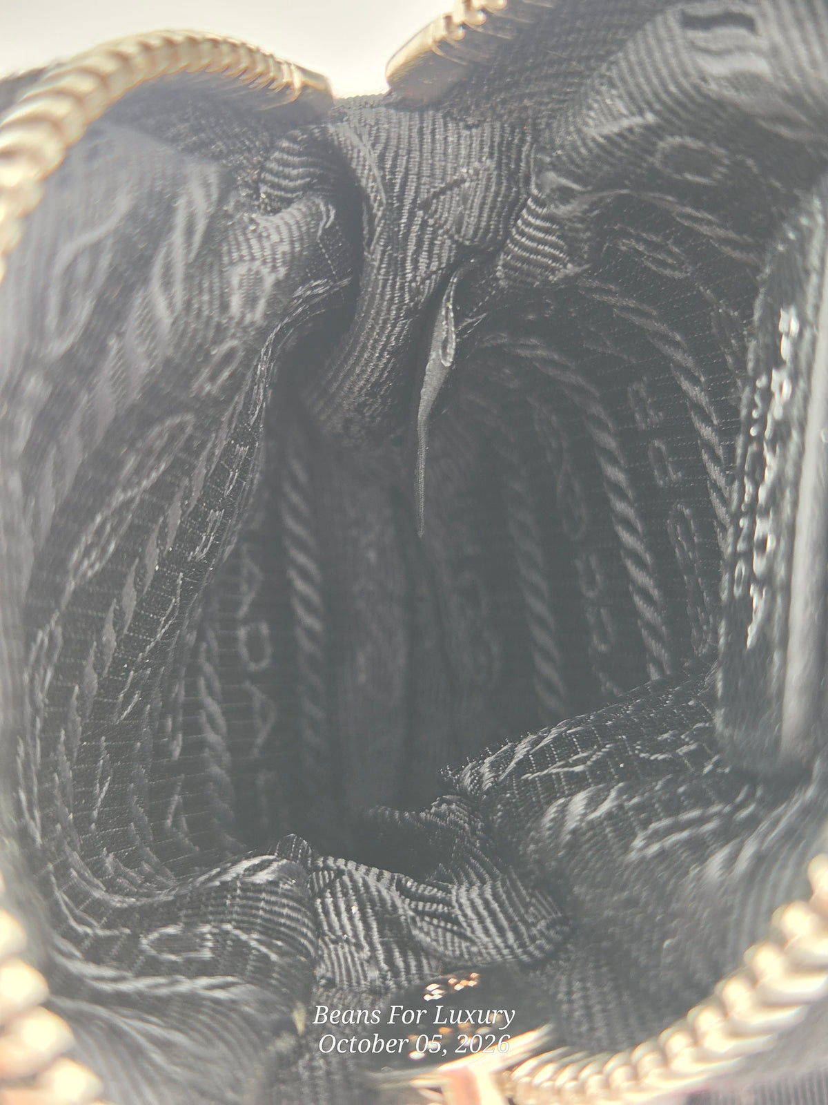 Close-up view of the interior lining of a black patterned handbag, showing a woven fabric lining with gold-toned zipper trim at the top and bottom. A small watermark at the bottom reads 'Beans For Luxury October 06, 2022'.