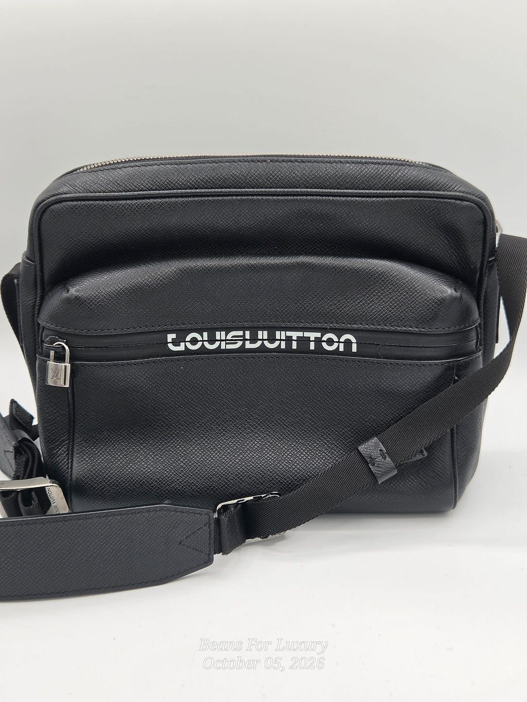 A black Louis Vuitton leather crossbody bag with a textured grain finish, featuring the brand name in white on the front pocket and a matching black shoulder strap.