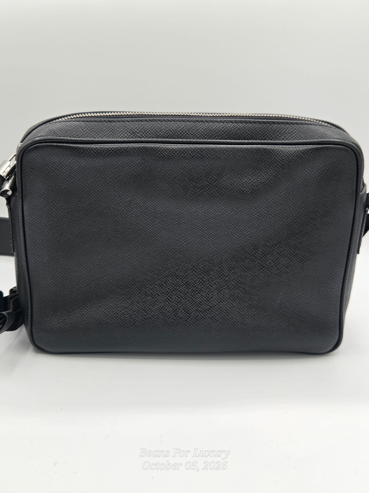 A black textured leather crossbody bag with a top zipper, shown against a plain light gray background.