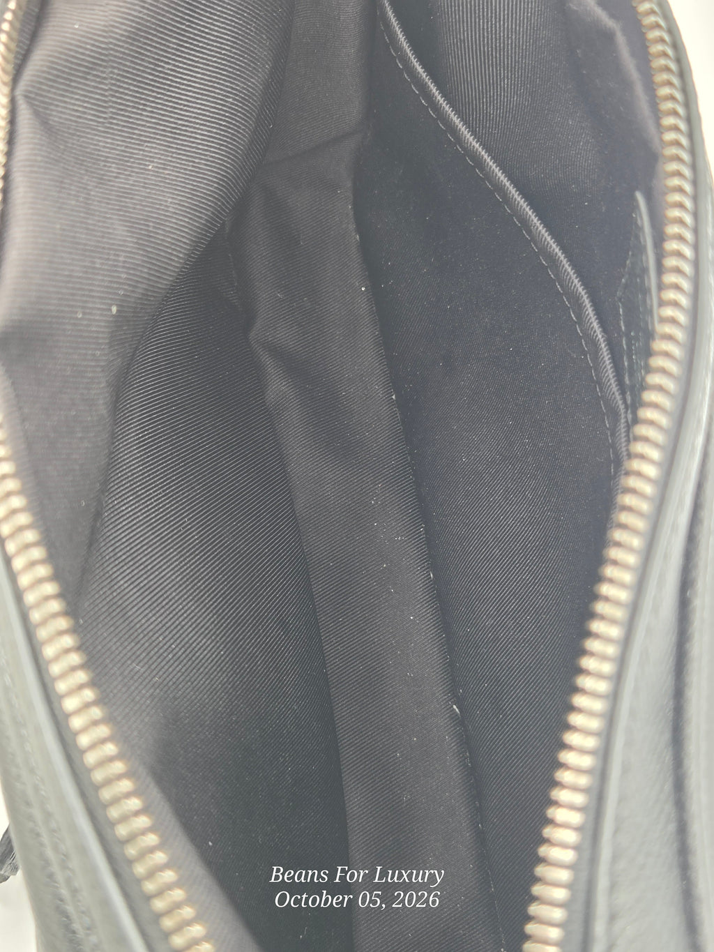 Close-up of the interior of a black bag or backpack, showing the black fabric lining, zipper tracks, and a small white text watermark at the bottom reading 'Beans For Luxury October 05, 2026'.