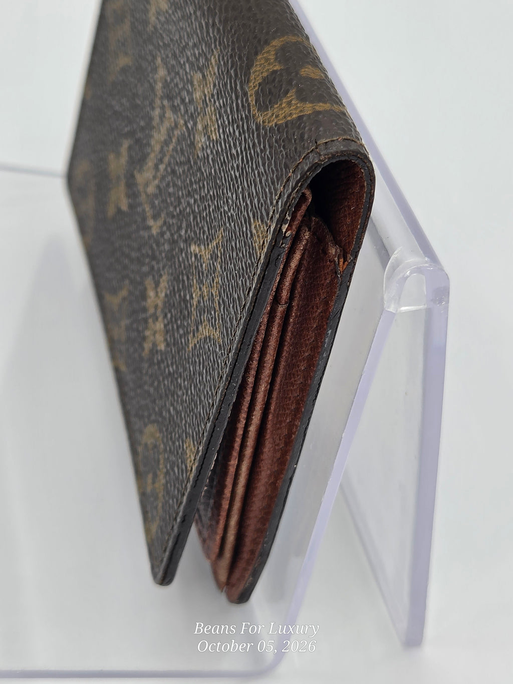 A close-up of a brown monogram card holder or wallet with a clear acrylic display stand against a white background.