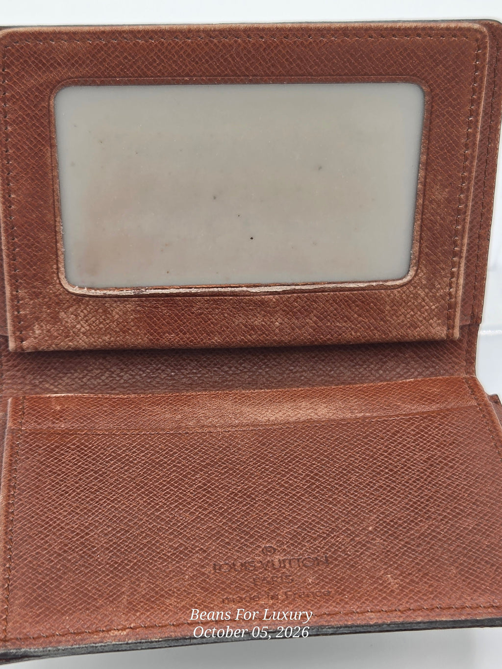 An open brown textured leather wallet or card holder with a clear ID window on the inside flap and card slots on the front, photographed against a white background.