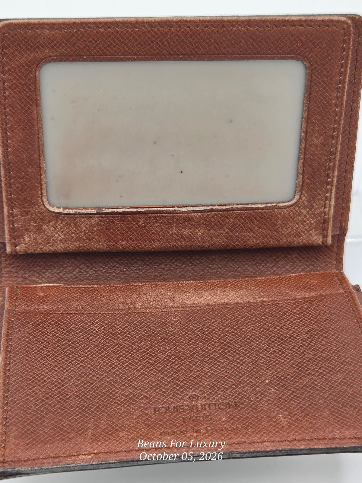 An open brown textured leather wallet or card holder with a clear ID window on the inside flap and card slots on the front, photographed against a white background.