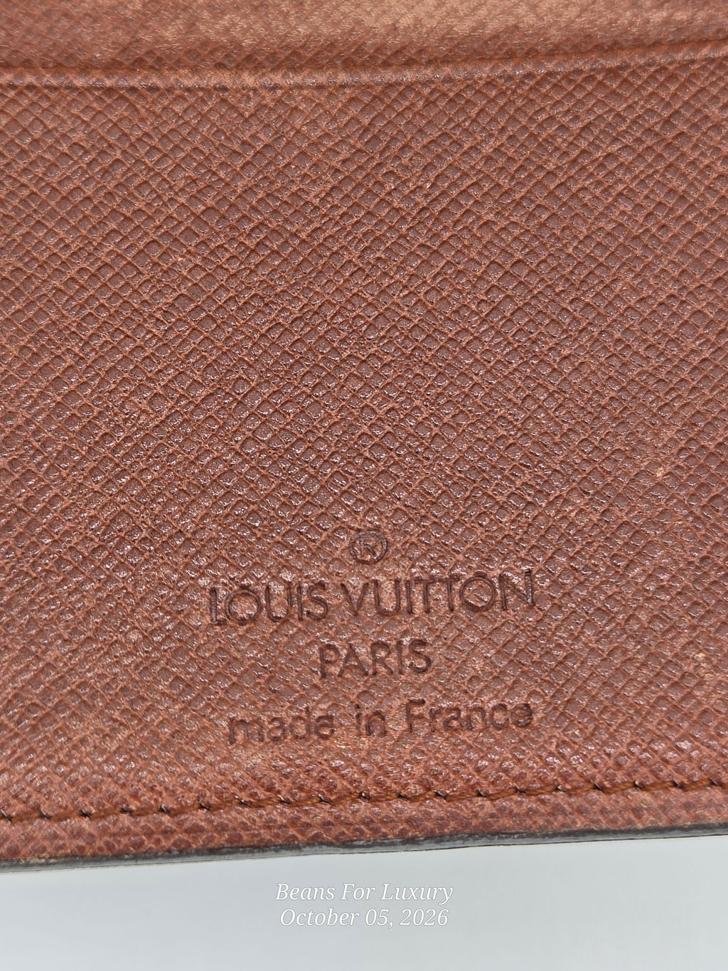 Close-up of a brown textured leather Louis Vuitton item with embossed 'LOUIS VUITTON PARIS made in France' text on a white surface.