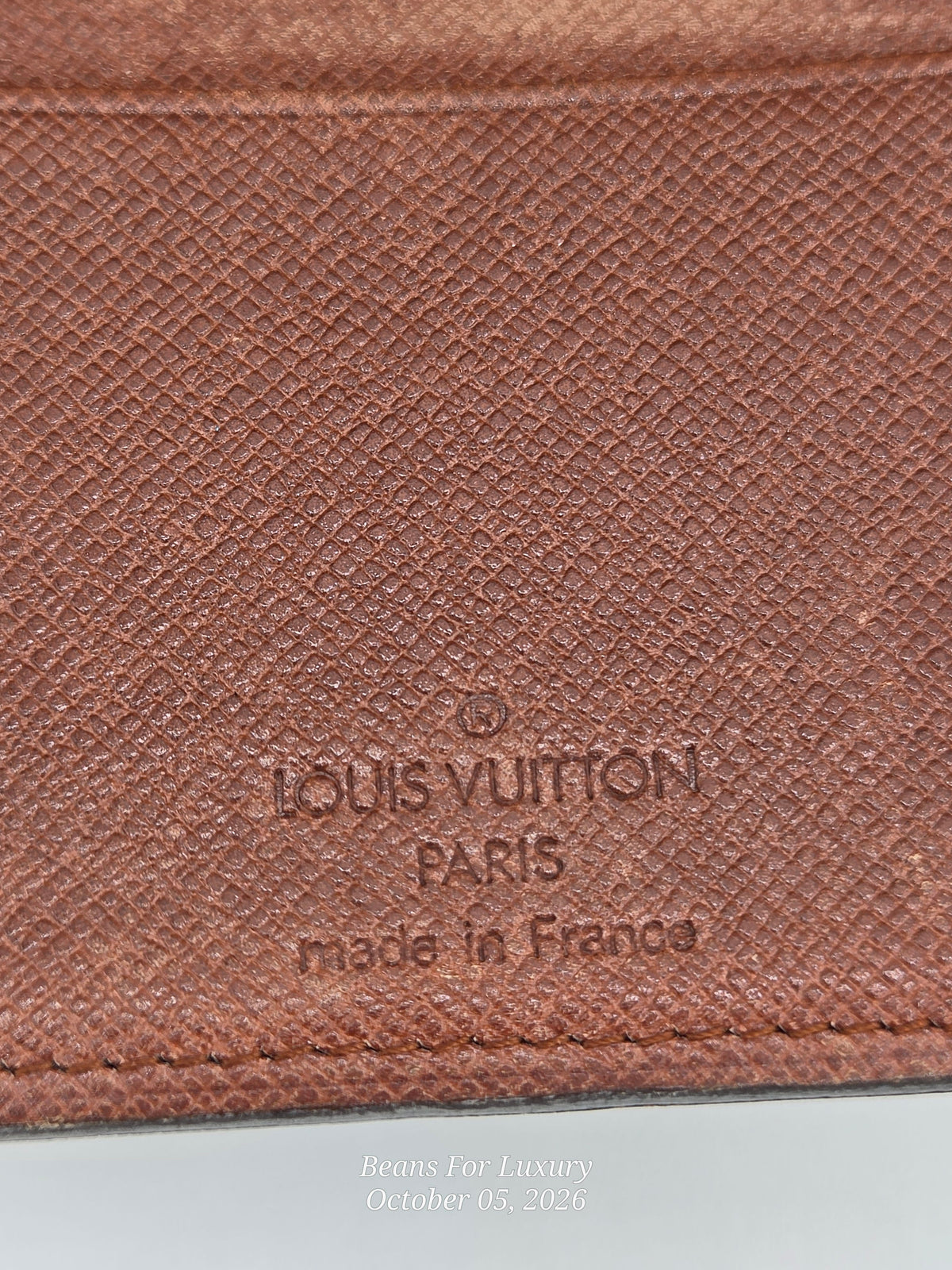 Close-up of a brown textured leather Louis Vuitton item with embossed 'LOUIS VUITTON PARIS made in France' text on a white surface.