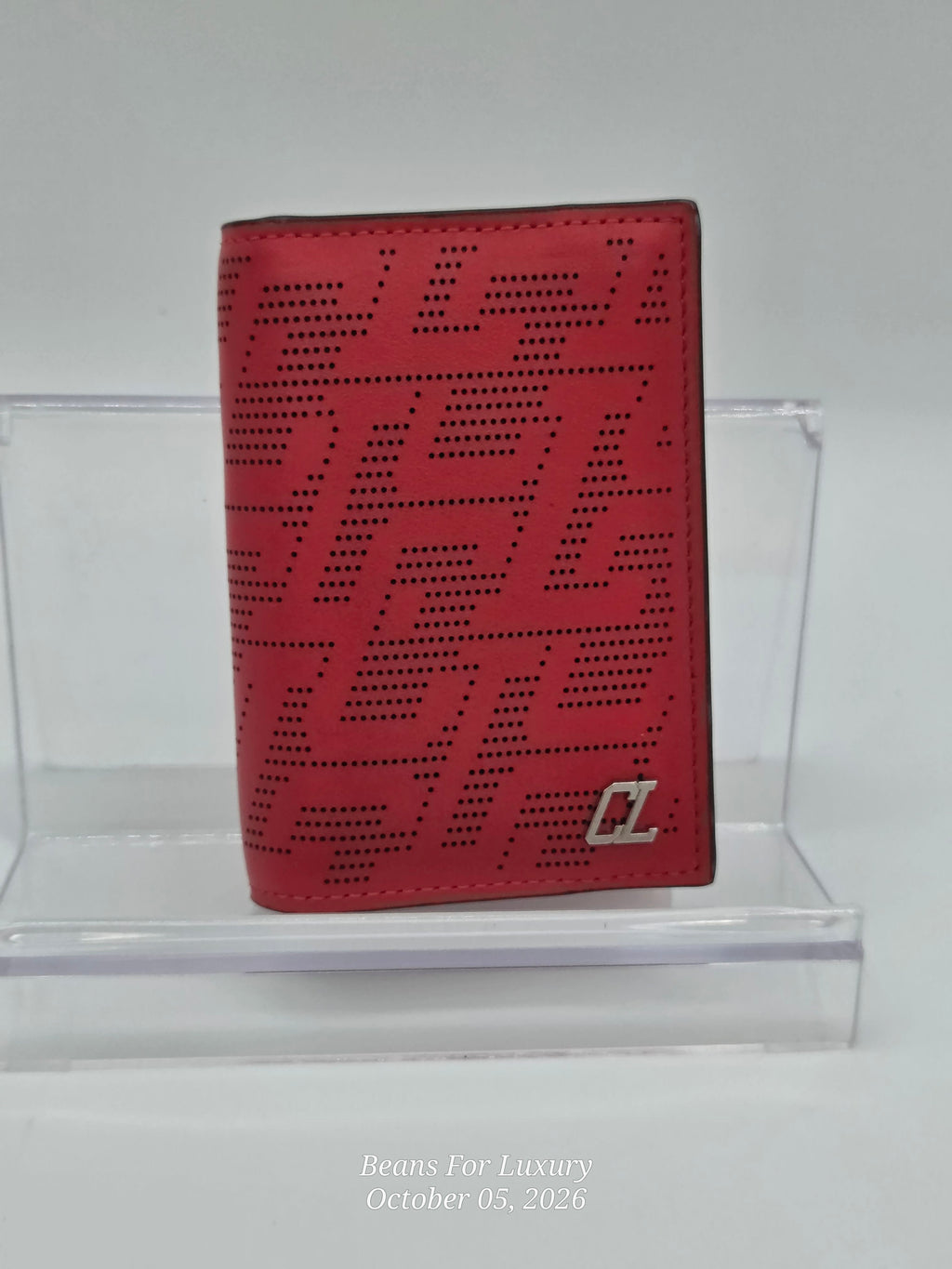 A red leather bifold wallet with a perforated geometric monogram pattern and a silver-toned 'Z' logo, displayed on a clear acrylic stand.