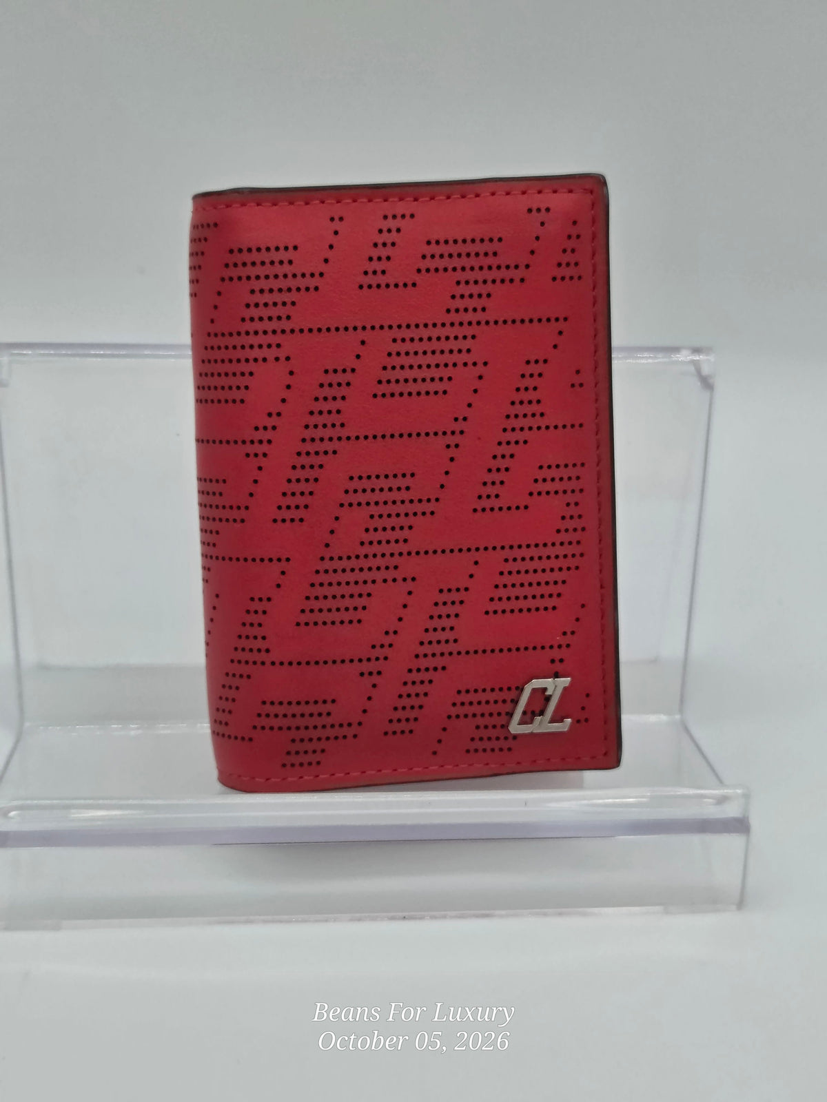 A red leather bifold wallet with a perforated geometric monogram pattern and a silver-toned 'Z' logo, displayed on a clear acrylic stand.