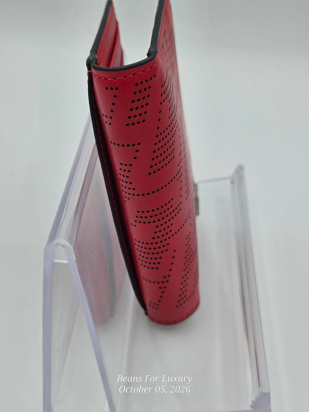 A red perforated leather wallet or card holder standing upright on a clear acrylic display stand against a white background.