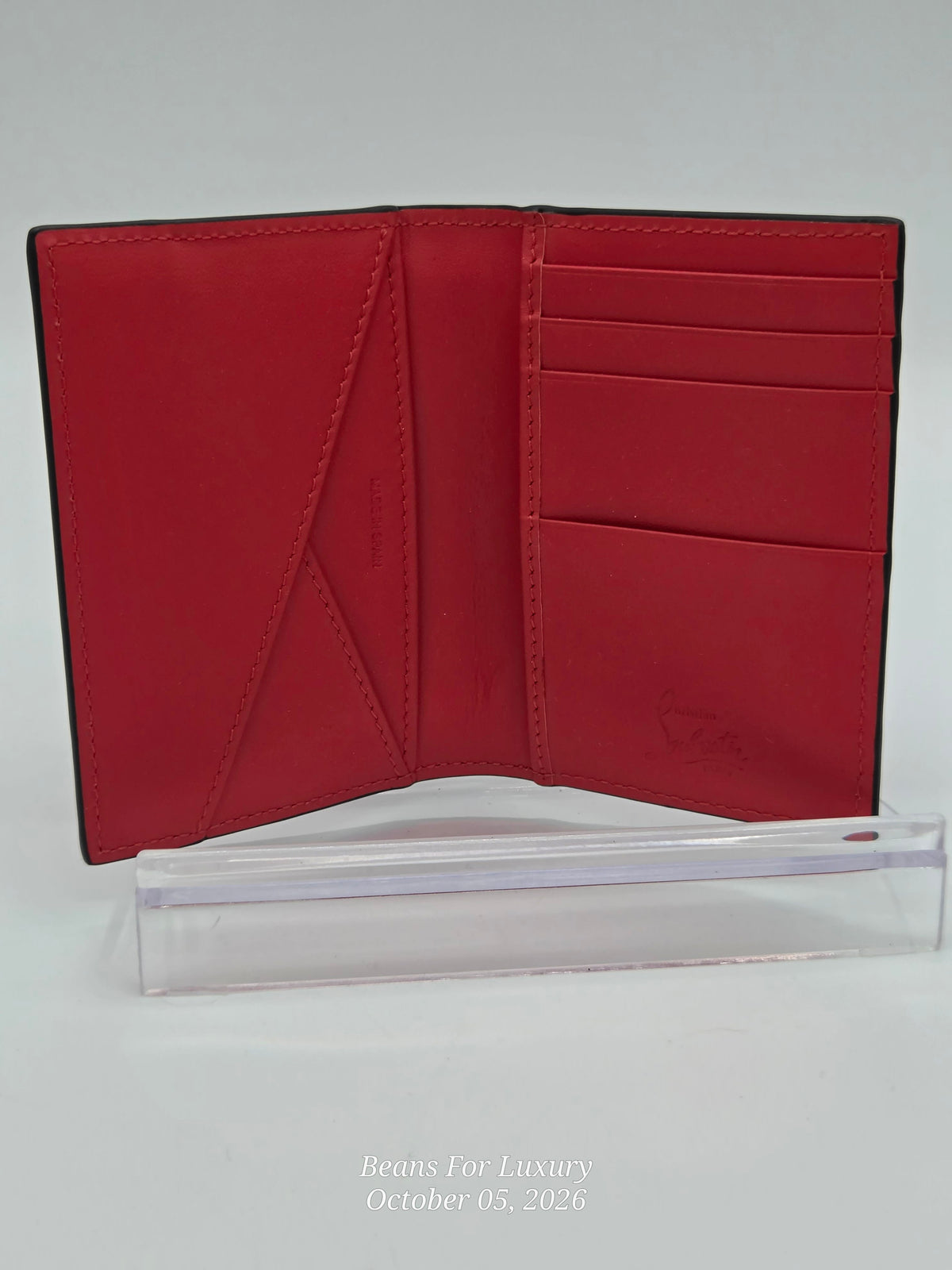 A red leather bifold wallet shown open, displaying its interior card slots and stitching, standing upright on a clear acrylic display block against a light gray background.