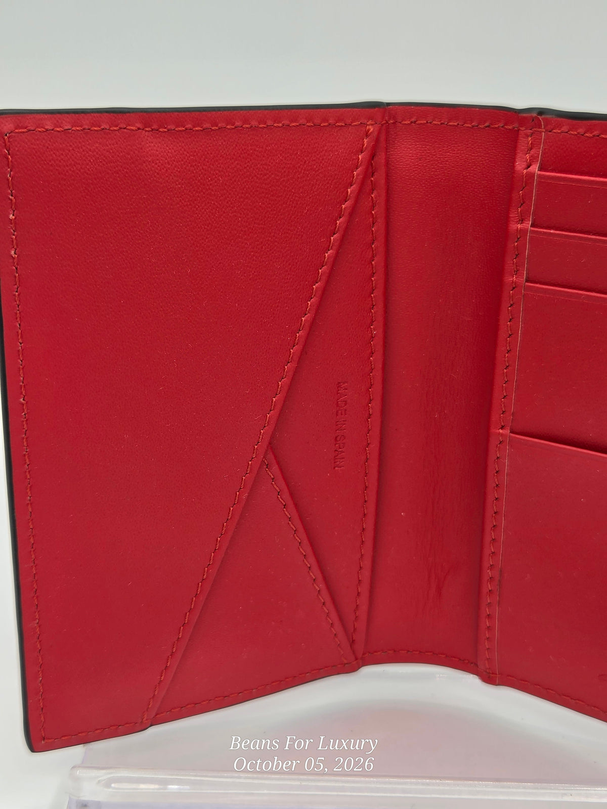 A close-up of an open red leather wallet showing the interior card slots and stitching, photographed against a light background.