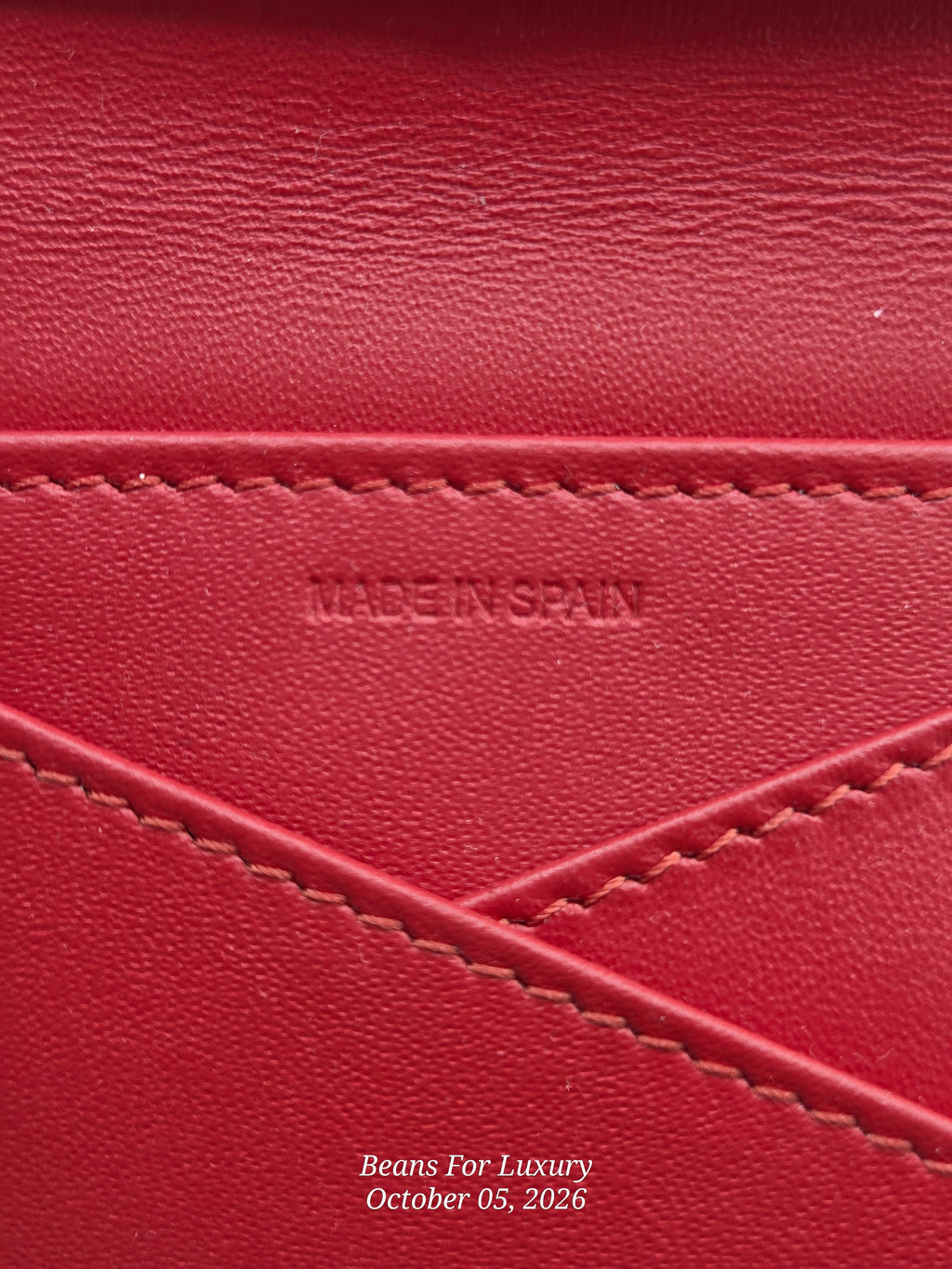 Close-up of a red leather surface with visible stitching and an embossed 'MADE IN SPAIN' mark, plus a small 'Beans For Luxury' watermark near the bottom.